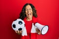 Middle age hispanic woman football hooligan holding ball and using megaphone smiling and laughing hard out loud because funny Royalty Free Stock Photo