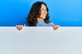 Middle age hispanic woman holding blank empty banner smiling looking to the side and staring away thinking