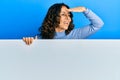 Middle age hispanic woman holding blank empty banner very happy and smiling looking far away with hand over head