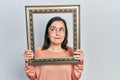 Middle age hispanic woman holding empty frame smiling looking to the side and staring away thinking Royalty Free Stock Photo