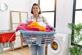 Middle age hispanic woman holding laundry basket smiling looking to the side and staring away thinking