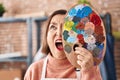 Middle age hispanic woman holding painter palette close to face angry and mad screaming frustrated and furious, shouting with Royalty Free Stock Photo