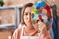 Middle age hispanic woman holding painter palette close to face depressed and worry for distress, crying angry and afraid Royalty Free Stock Photo