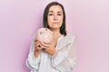 Middle age hispanic woman holding piggy bank relaxed with serious expression on face Royalty Free Stock Photo