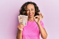 Middle age hispanic woman holding united kingdom pounds doing ok sign with fingers, smiling friendly gesturing excellent symbol