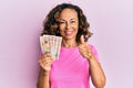 Middle age hispanic woman holding united kingdom pounds smiling happy and positive, thumb up doing excellent and approval sign