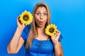 Middle age hispanic woman holding yellow sunflowers afraid and shocked with surprise and amazed expression, fear and excited face Royalty Free Stock Photo