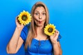 Middle age hispanic woman holding yellow sunflowers making fish face with mouth and squinting eyes, crazy and comical Royalty Free Stock Photo