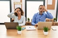 Middle age hispanic woman and man sitting with laptop at the office doing ok gesture shocked with surprised face, eye looking Royalty Free Stock Photo