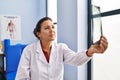 Middle age hispanic woman physiotherapist holding radiography at rehab clinic