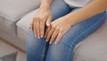 Middle age hispanic woman sitting on sofa with hands on knees at home