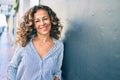 Middle age hispanic woman smiling happy leaning on the wall at the city