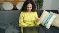 Middle age hispanic woman using laptop and credit card sitting on sofa at home Royalty Free Stock Photo