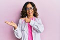 Middle age hispanic woman wearing doctor uniform and glasses amazed and smiling to the camera while presenting with hand and