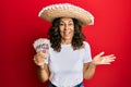 Middle age hispanic woman wearing mexican hat holding pesos banknotes celebrating achievement with happy smile and winner Royalty Free Stock Photo