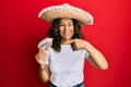 Middle age hispanic woman wearing mexican hat holding pesos banknotes smiling happy pointing with hand and finger Royalty Free Stock Photo