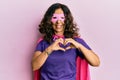 Middle age hispanic woman wearing super hero costume smiling in love doing heart symbol shape with hands