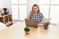 Middle age hispanic woman working at the office with laptop speaking on the phone clueless and confused expression Royalty Free Stock Photo