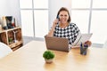 Middle age hispanic woman working at the office with laptop speaking on the phone sticking tongue out happy with funny expression Royalty Free Stock Photo