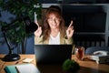 Middle age hispanic woman working using computer laptop at night gesturing finger crossed smiling with hope and eyes closed