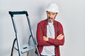 Middle age hispanic worker man with arms crossed gesture using ladder in shock face, looking skeptical and sarcastic, surprised Royalty Free Stock Photo