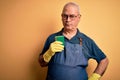 Middle age hoary cleaner man cleaning wearing apron and gloves using scourer with a confident expression on smart face thinking