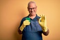 Middle age hoary cleaner man cleaning wearing apron and gloves using scourer doing ok sign with fingers, excellent symbol