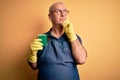 Middle age hoary cleaner man cleaning wearing apron and gloves using scourer serious face thinking about question, very confused