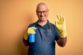 Middle age hoary cleaner man cleaning wearing apron and gloves using sprayer doing ok sign with fingers, excellent symbol