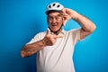 Middle age hoary cyclist man wearing bike security helmet over isolated blue background smiling making frame with hands and