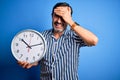 Middle age hoary man holding big clock standing over isolated blue background stressed with hand on head, shocked with shame and Royalty Free Stock Photo