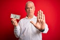 Middle age hoary man holding one dollar banknote over isolated red background with open hand doing stop sign with serious and Royalty Free Stock Photo