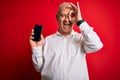 Middle age hoary man holding smartphone showing screen over isolated red background with happy face smiling doing ok sign with Royalty Free Stock Photo