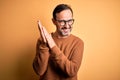 Middle age hoary man wearing brown sweater and glasses over isolated yellow background clapping and applauding happy and joyful, Royalty Free Stock Photo