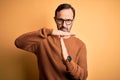 Middle age hoary man wearing brown sweater and glasses over isolated yellow background Doing time out gesture with hands,