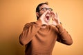 Middle age hoary man wearing brown sweater and glasses over isolated yellow background Shouting angry out loud with hands over