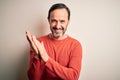 Middle age hoary man wearing casual orange sweater standing over isolated white background clapping and applauding happy and