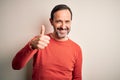 Middle age hoary man wearing casual orange sweater standing over isolated white background doing happy thumbs up gesture with hand