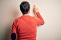 Middle age hoary man wearing casual orange sweater standing over isolated white background Posing backwards pointing ahead with