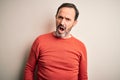 Middle age hoary man wearing casual orange sweater standing over isolated white background In shock face, looking skeptical and Royalty Free Stock Photo