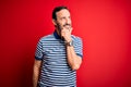 Middle age hoary man wearing casual striped polo standing over isolated red background with hand on chin thinking about question,