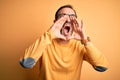 Middle age hoary man wearing casual sweater and glasses over isolated yellow background Shouting angry out loud with hands over