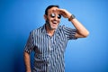 Middle age hoary man wearing striped shirt and sunglasses over isolated blue background very happy and smiling looking far away