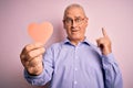 Middle age hoary romantic man holding red paper heart shape over isolated pink background surprised with an idea or question Royalty Free Stock Photo