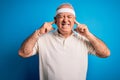 Middle age hoary sportsman doing sport wearing sportswear over isolated blue background covering ears with fingers with annoyed