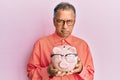 Middle age indian man holding piggy bank with glasses depressed and worry for distress, crying angry and afraid Royalty Free Stock Photo