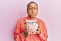 Middle age indian man holding piggy bank with glasses puffing cheeks with funny face