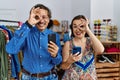 Middle age interracial couple at retail shop using smartphone doing ok gesture with hand smiling, eye looking through fingers with Royalty Free Stock Photo