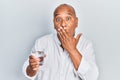 Middle age latin man drinking glass of water covering mouth with hand, shocked and afraid for mistake