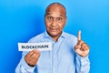 Middle age latin man holding paper with blockchain message smiling with an idea or question pointing finger with happy face,